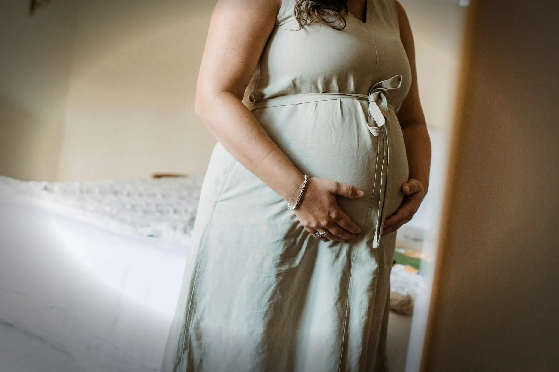 Faceless crop adult pregnant female standing near mirror in room while touching stomach in daytime